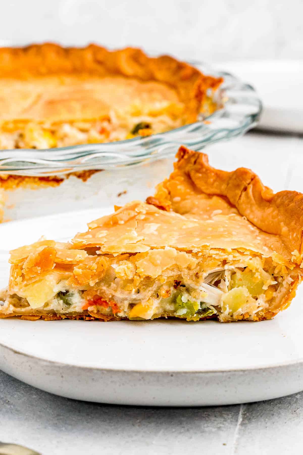 In the background, the baked chicken pot pie. In the foreground, a slice of the pie on a plate with a fork.