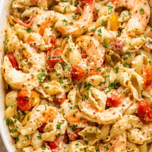 white baking dish with shrimp and pasta tossed with a cream cheese sauce and cherry tomatoes