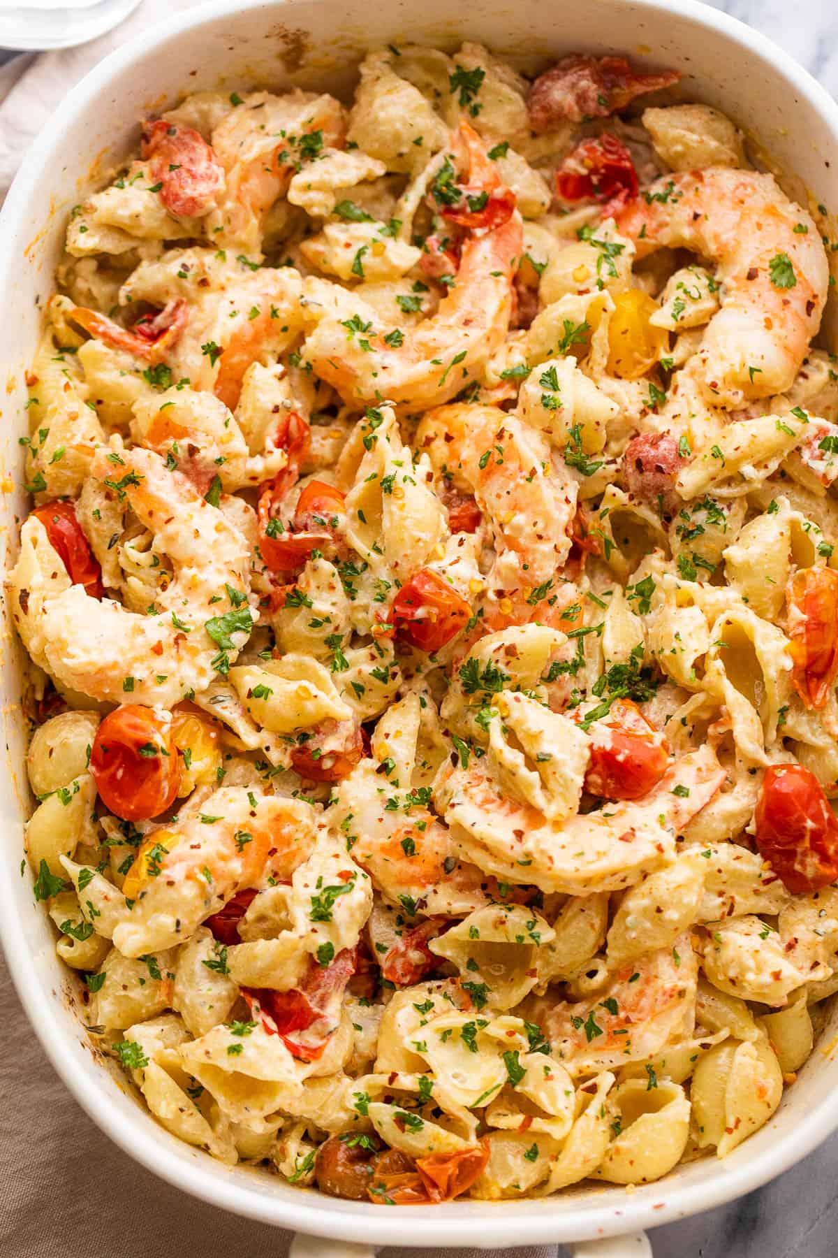 white baking dish with shrimp and pasta tossed with a cream cheese sauce and cherry tomatoes