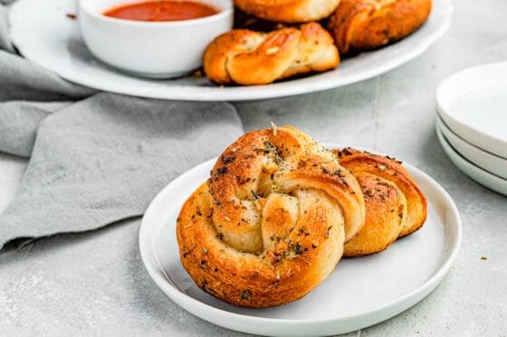 A wide shot of garlic knots piled onto a plate with marinara dipping sauce on the side.