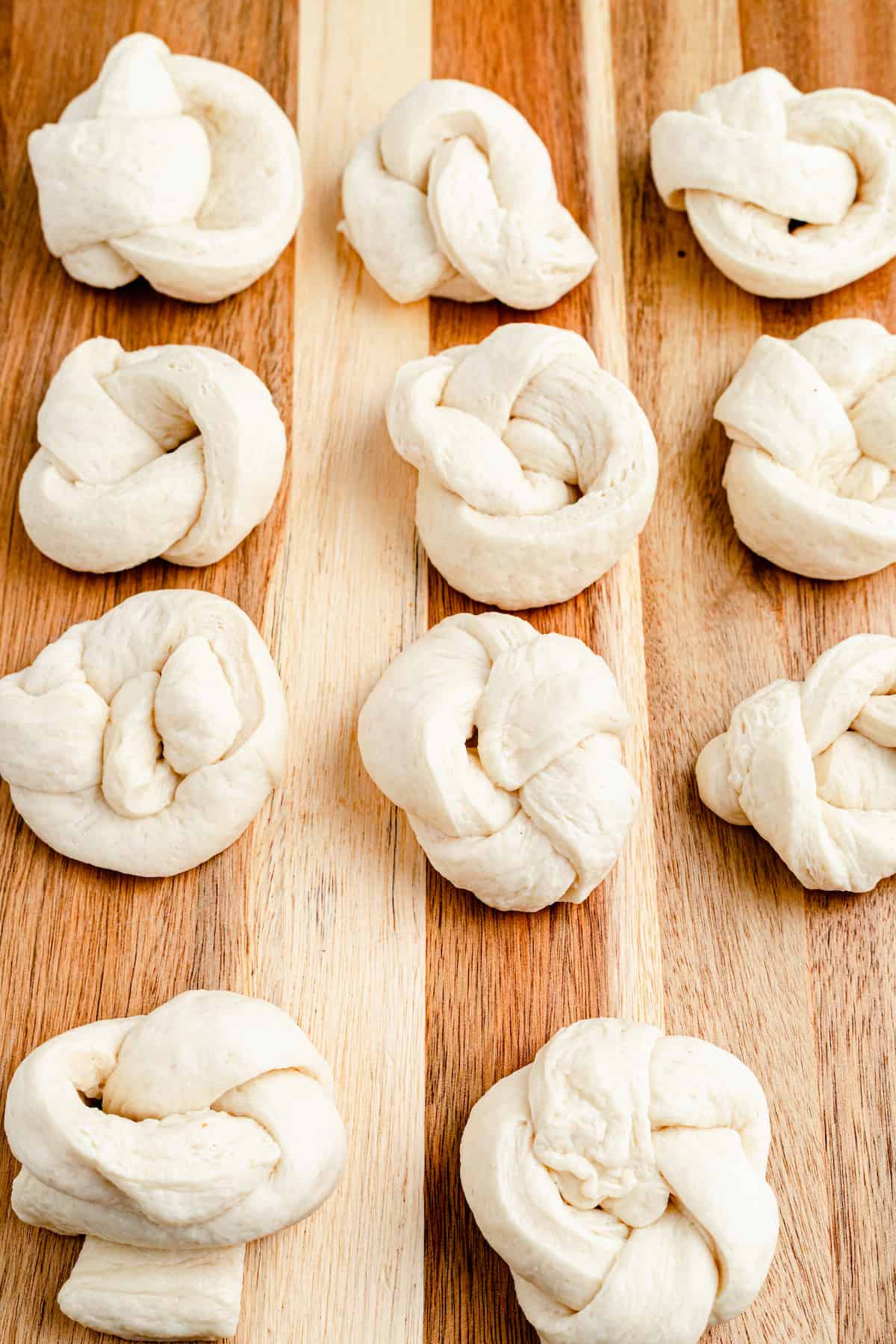 Unbaked and unseasoned strips of pizza dough, shaped into knots on a work surface.