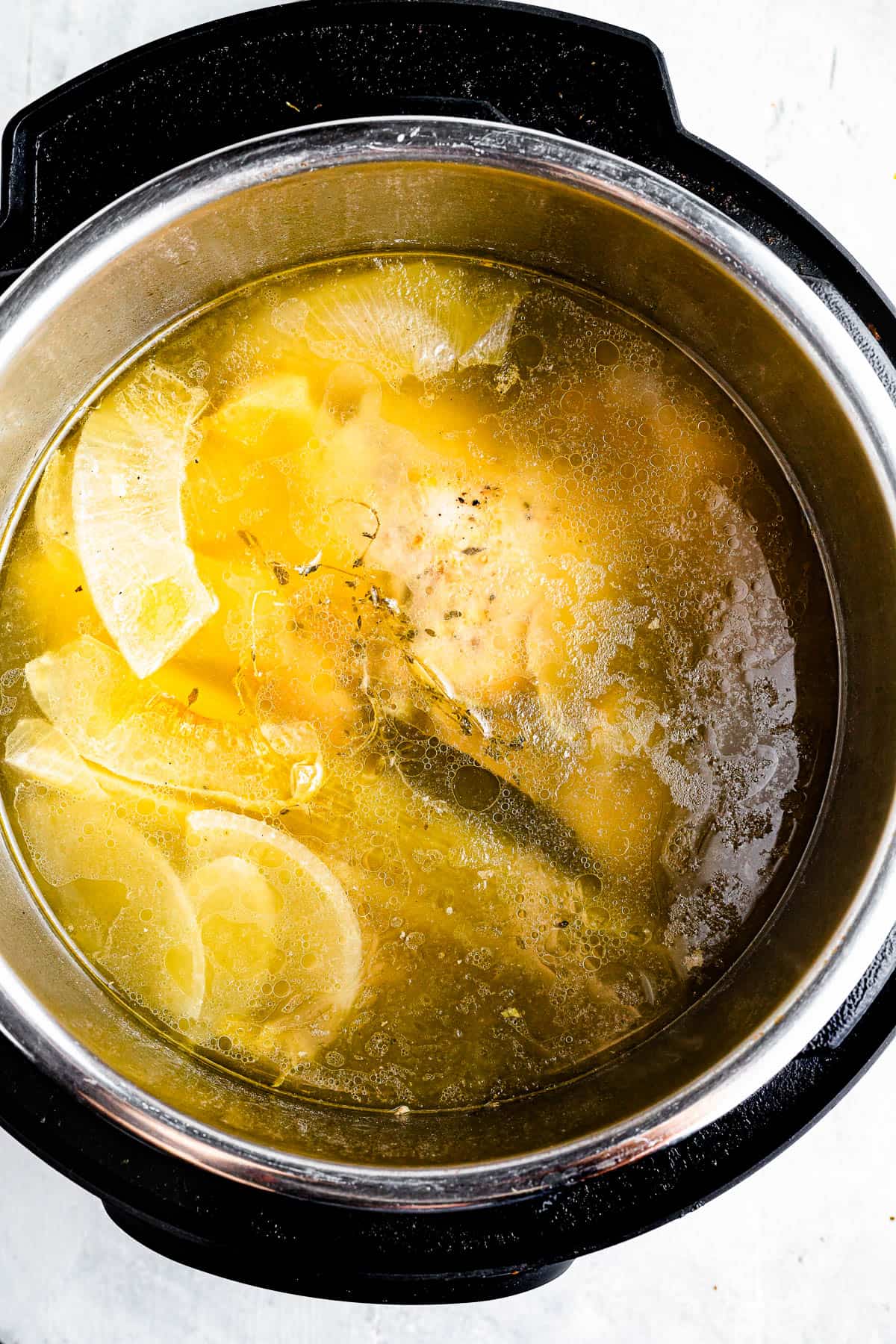 An overhead shot of the interior of an Instant Pot, filled with chicken broth, a cooked chicken, and scraps of vegetables.