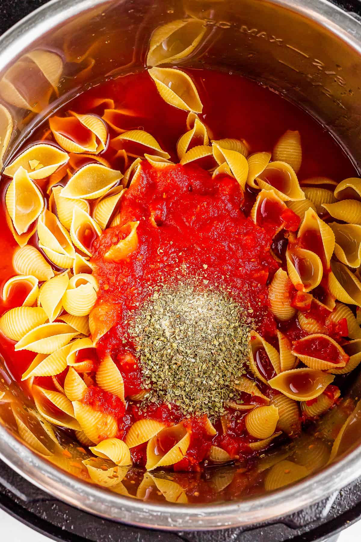 An overhead shot of an Instant Pot with crushed tomatoes, water, pasta, and seasonings inside.