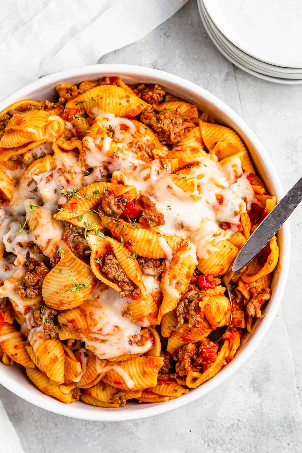 A serving dish filled with cooked pasta shells and ground beef in tomato sauce, topped with melted mozzarella.