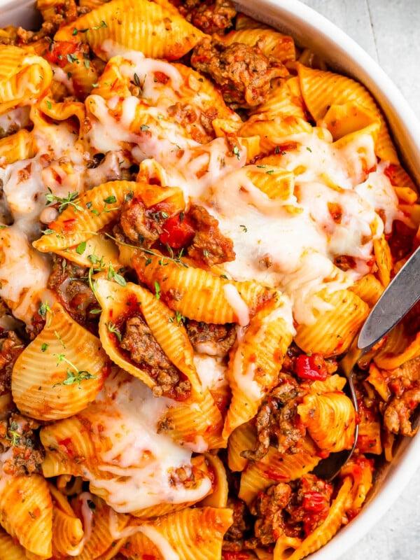 A serving dish filled with cooked pasta shells and ground beef in tomato sauce, topped with melted mozzarella.