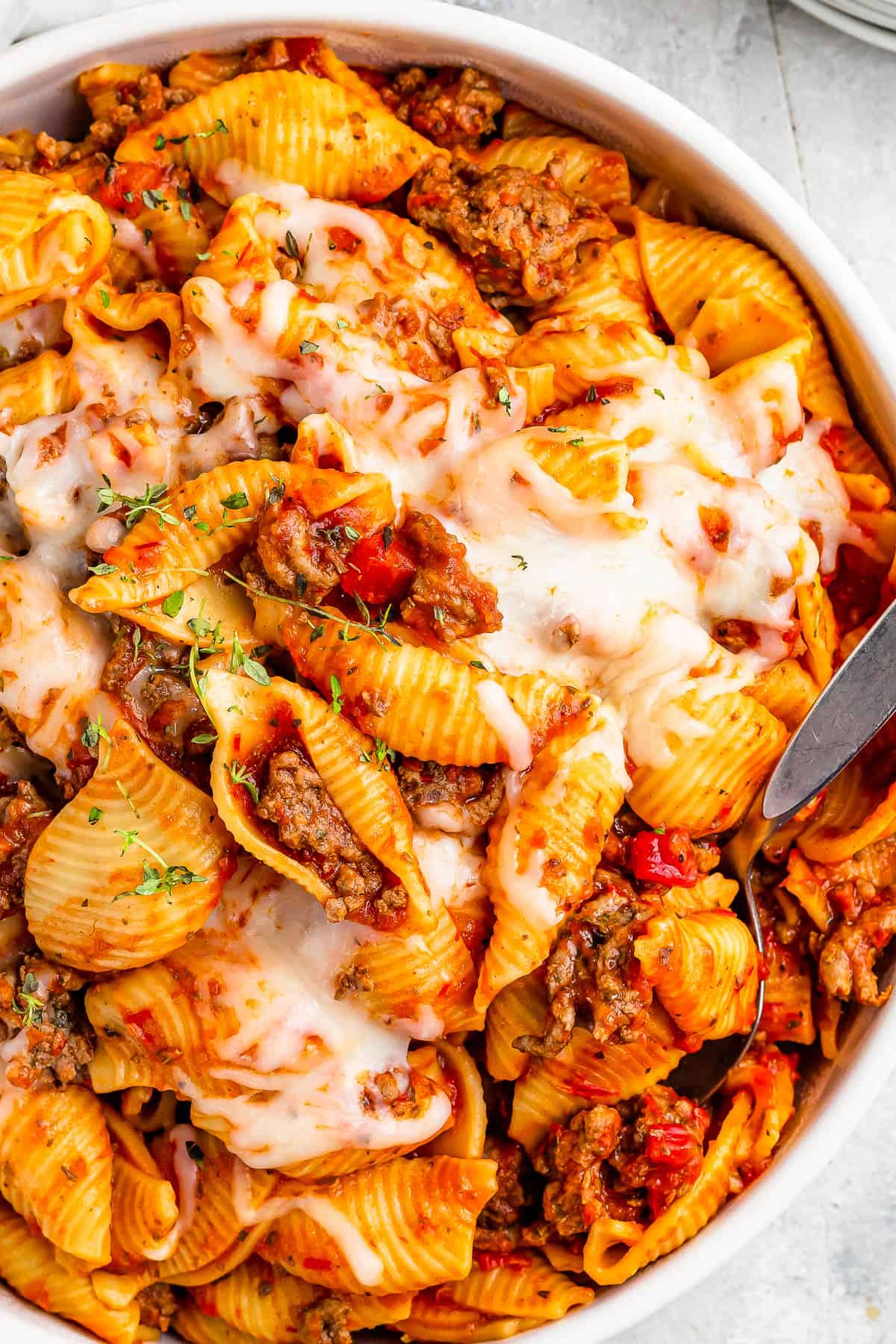 A serving dish filled with cooked pasta shells and ground beef in tomato sauce, topped with melted mozzarella.