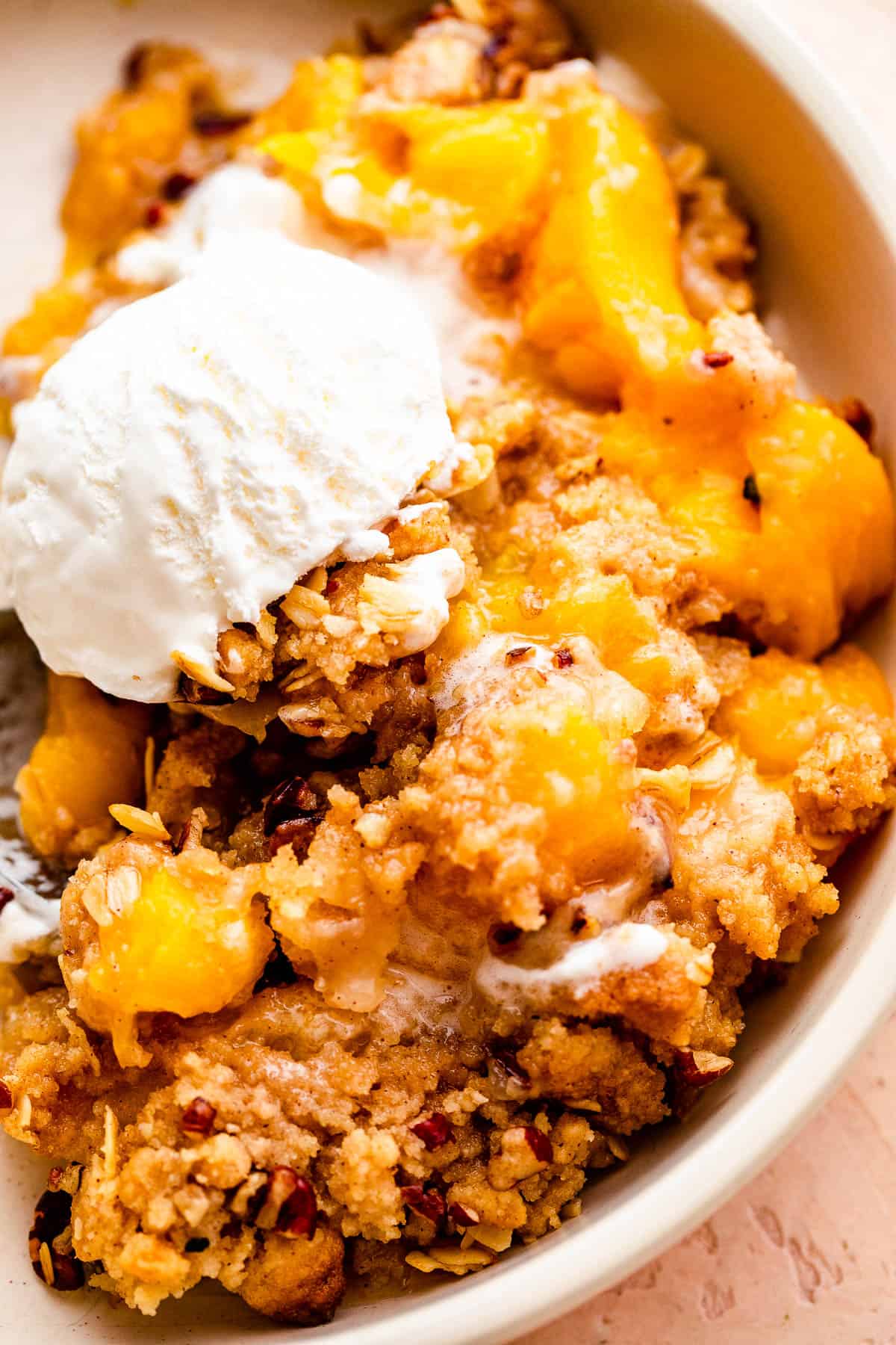 bowl of peach crisp topped with a scoop of vanilla ice cream