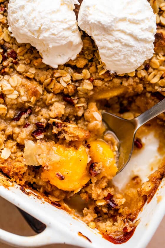 peach crisp in a white baking dish topped with scoops of vanilla ice cream
