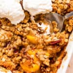 peach crisp in a white baking dish topped with three scoops of vanilla ice cream