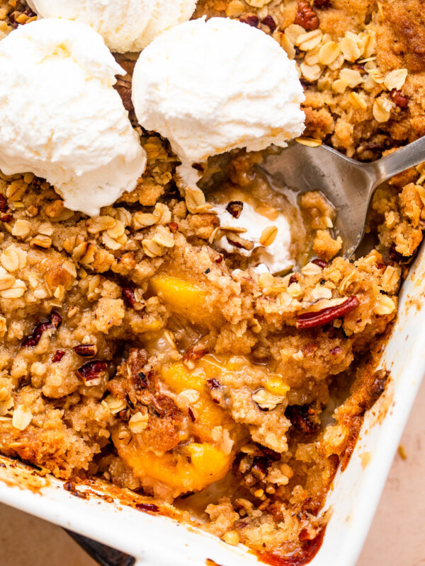 peach crisp in a white baking dish topped with three scoops of vanilla ice cream