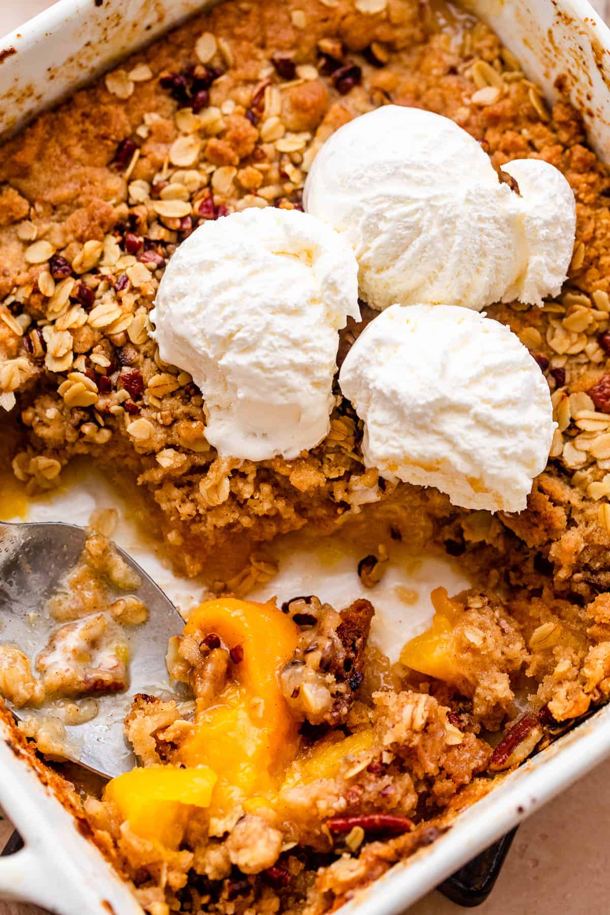peach crisp in a white baking dish topped with scoops of vanilla ice cream
