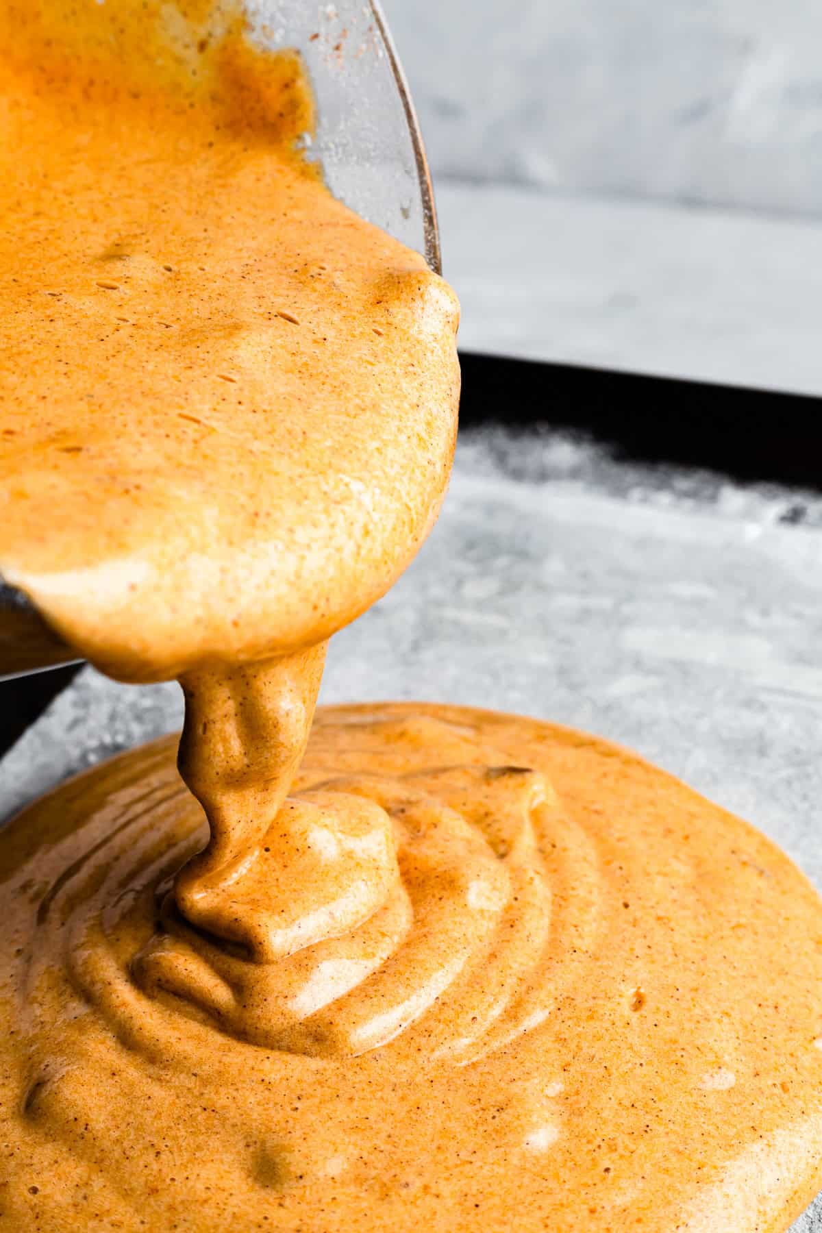 Pouring cake batter into a parchment paper-lined baking sheet.