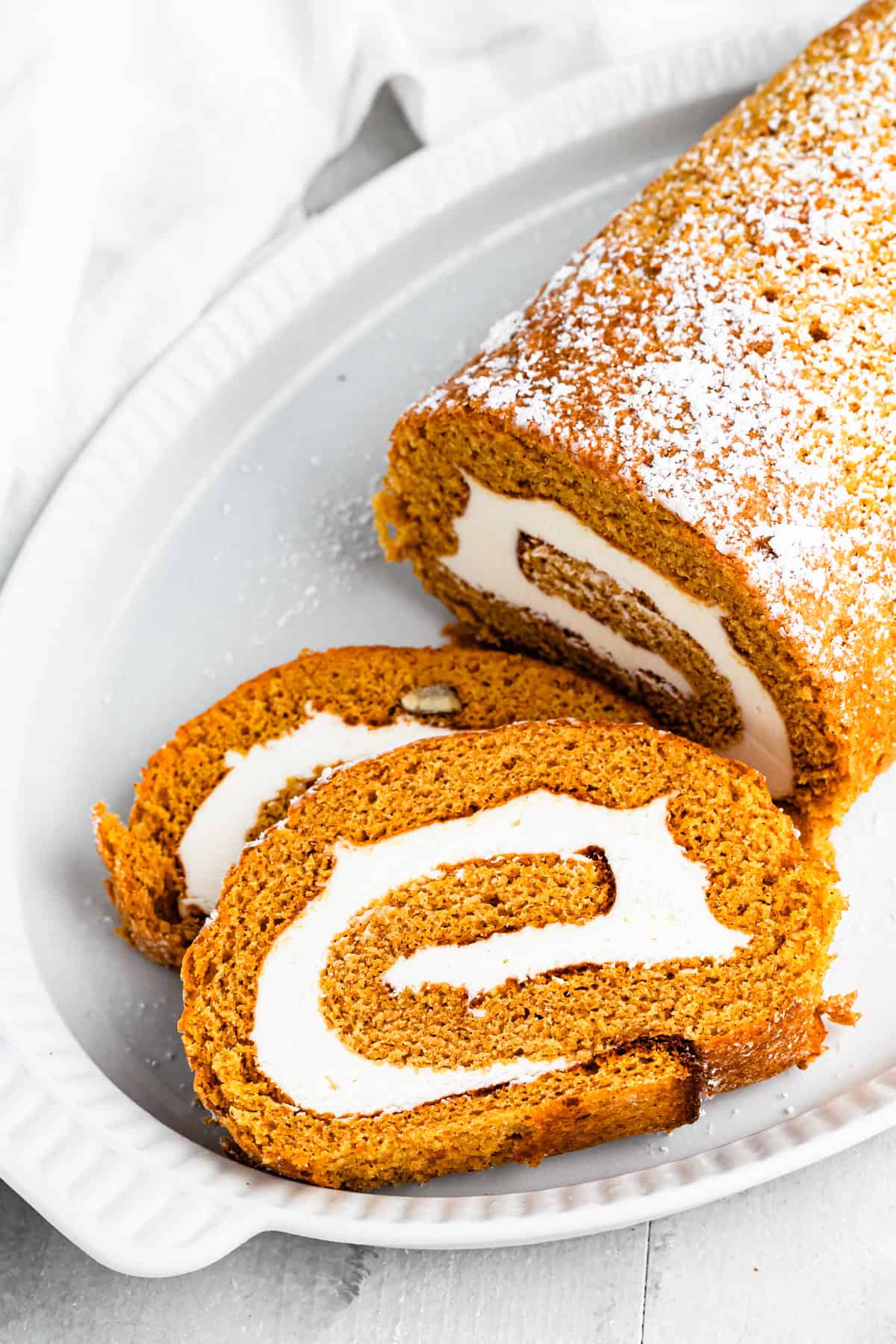 A pumpkin roll served on a plate with one slice cut out.