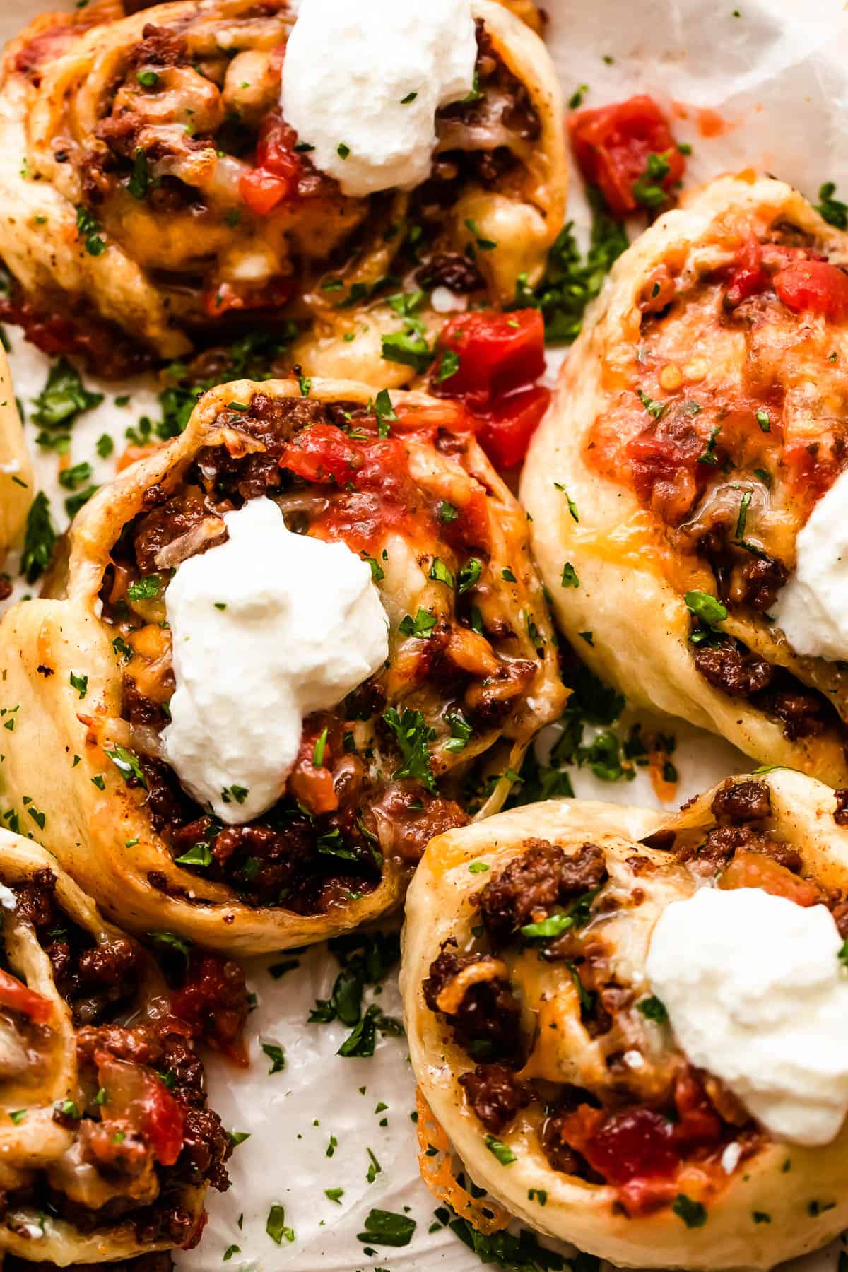 overhead shot of taco pinwheels topped with diced tomatoes and sour cream.