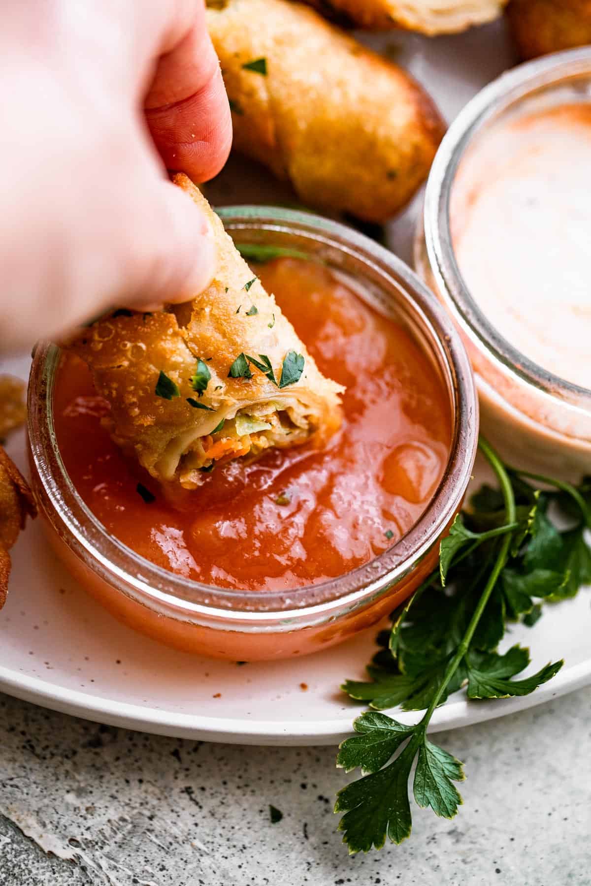 A small plate of spring rolls and dipping sauce, with one spring roll partially dipped in the sauce.