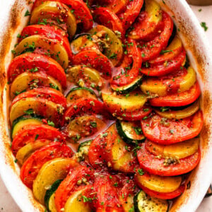 overhead shot of zucchini, tomato, and potato slices arranged accordion style in a baking dish.