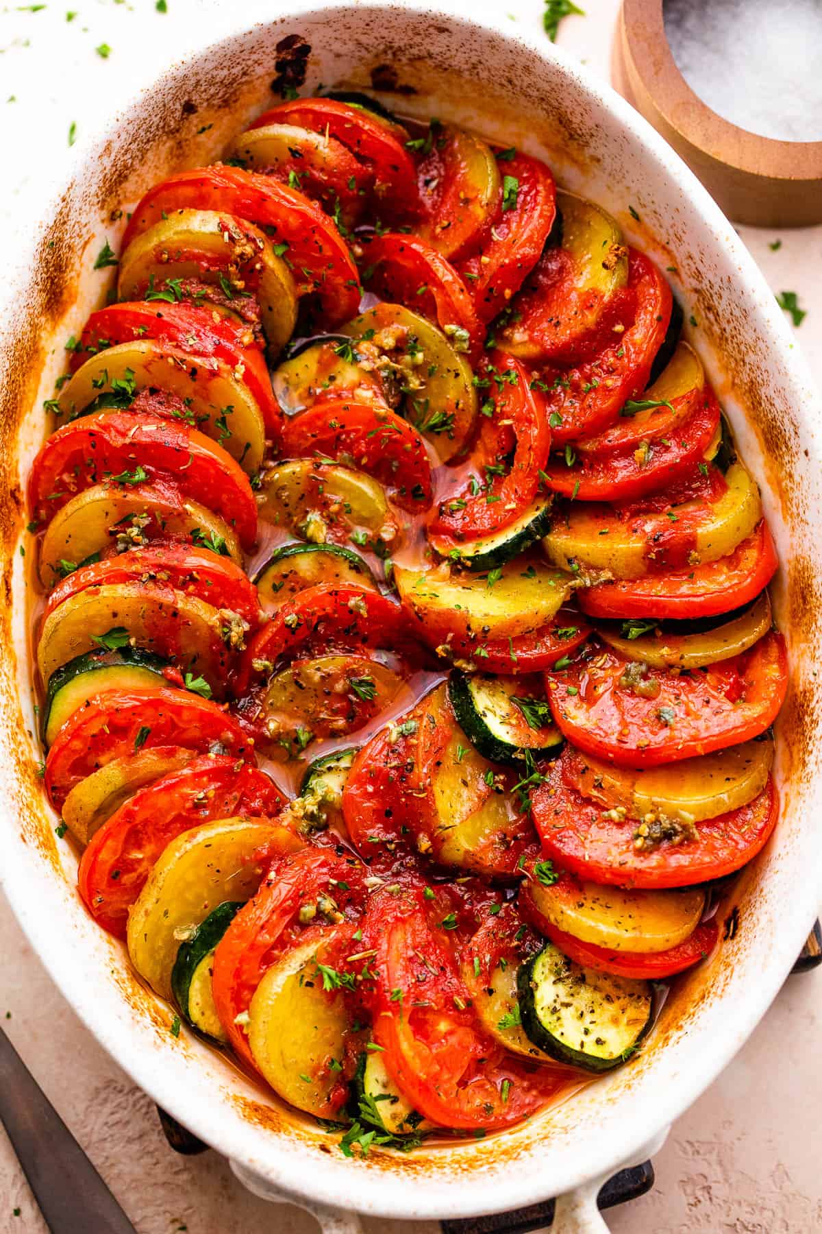 overhead shot of zucchini, tomato, and potato slices arranged accordion style in a baking dish.