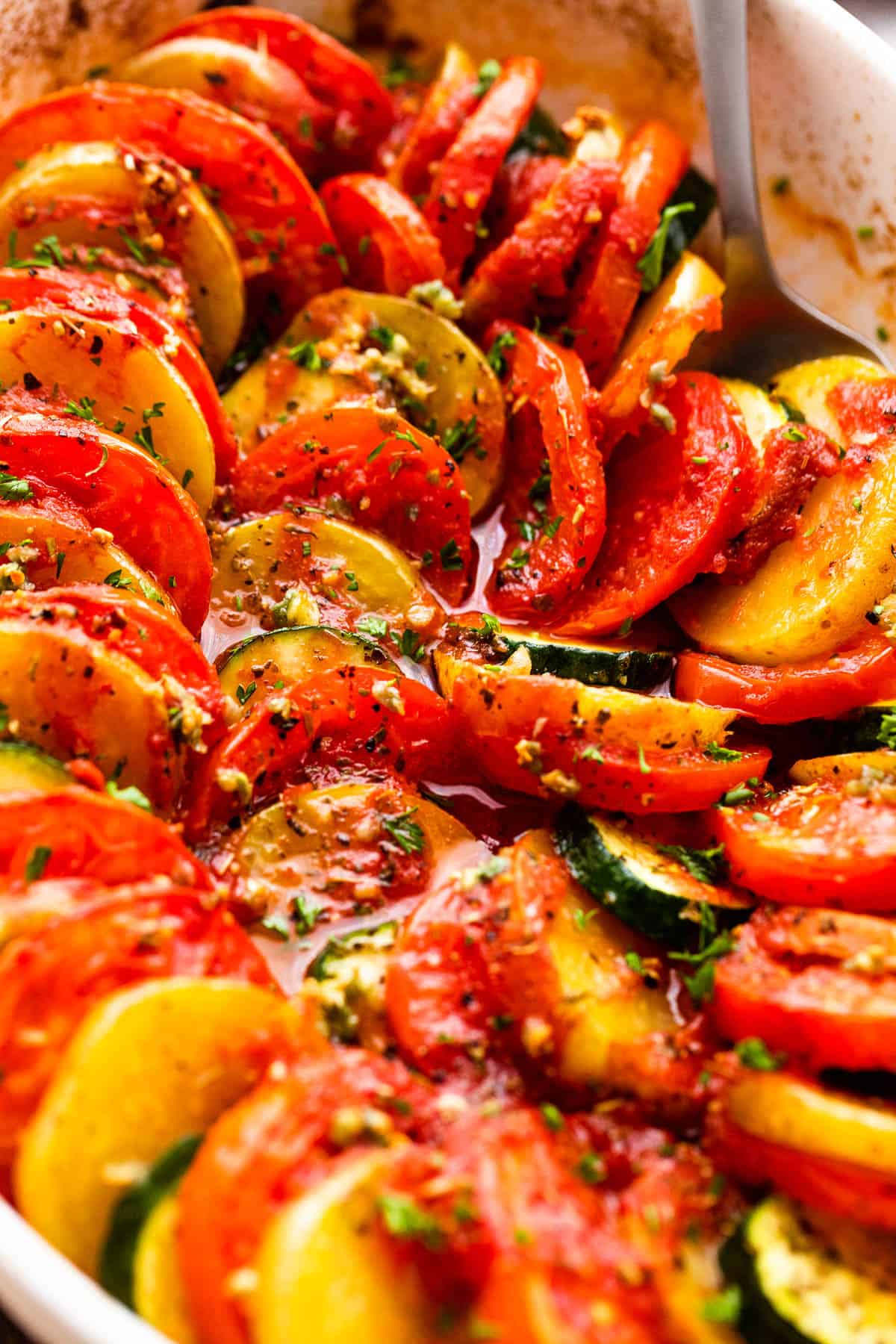 close up shot of zucchini slices, tomato slices, and potato slices arranged accordion style in a baking dish.