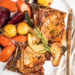 A plate of baked pork chops with apples and winter vegetables, garnished with a sprig of rosemary.