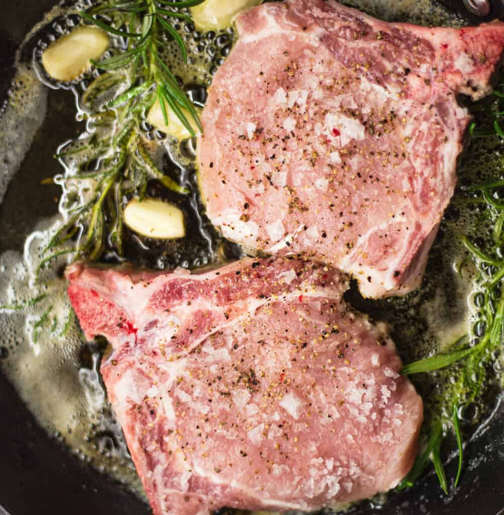 Searing pork chops in a skillet with garlic and rosemary.