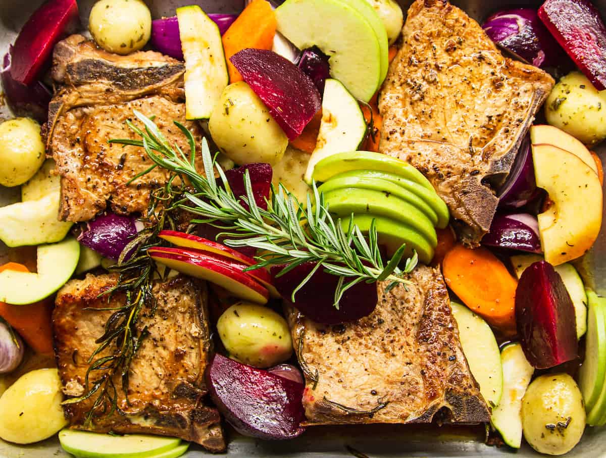 A close-up overhead shot of the baking dish with pork chops, apples, and vegetables cooked with apple juice and rosemary.