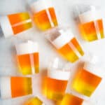 10 candy-corn jello shots scattered on a white table.