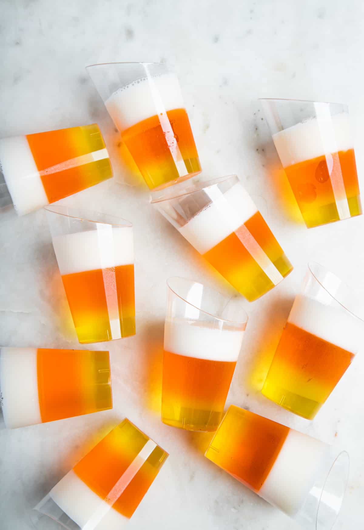 10 candy-corn jello shots scattered on a white table.