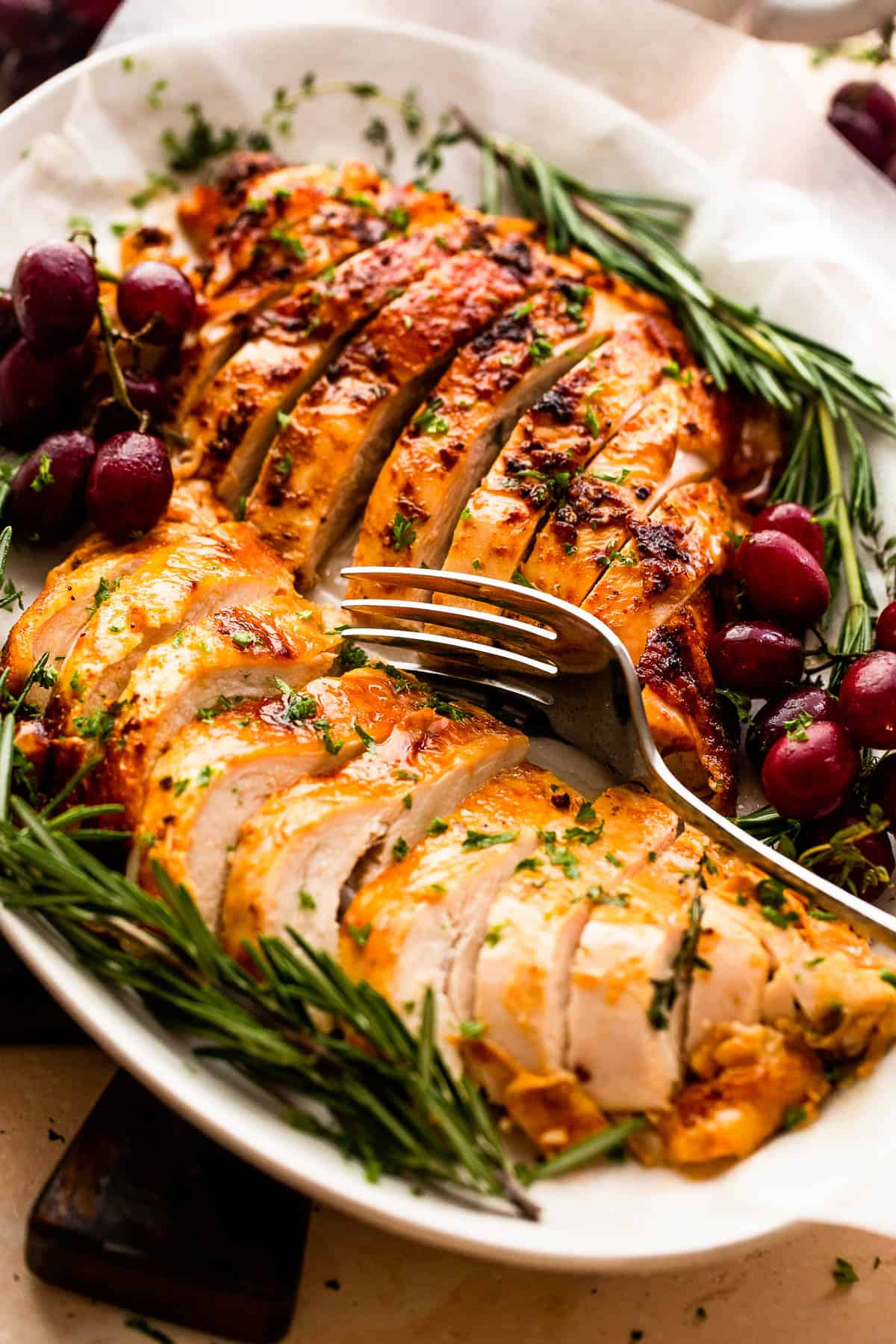 two turkey breasts sliced and arranged on a platter with rosemary and grape garnish