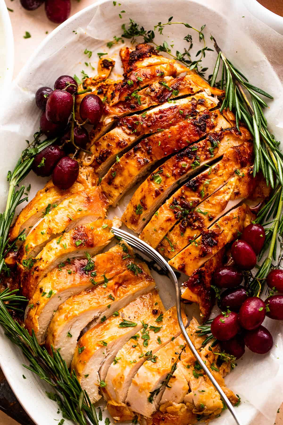 two turkey breasts sliced and arranged on a platter with rosemary and grape garnish
