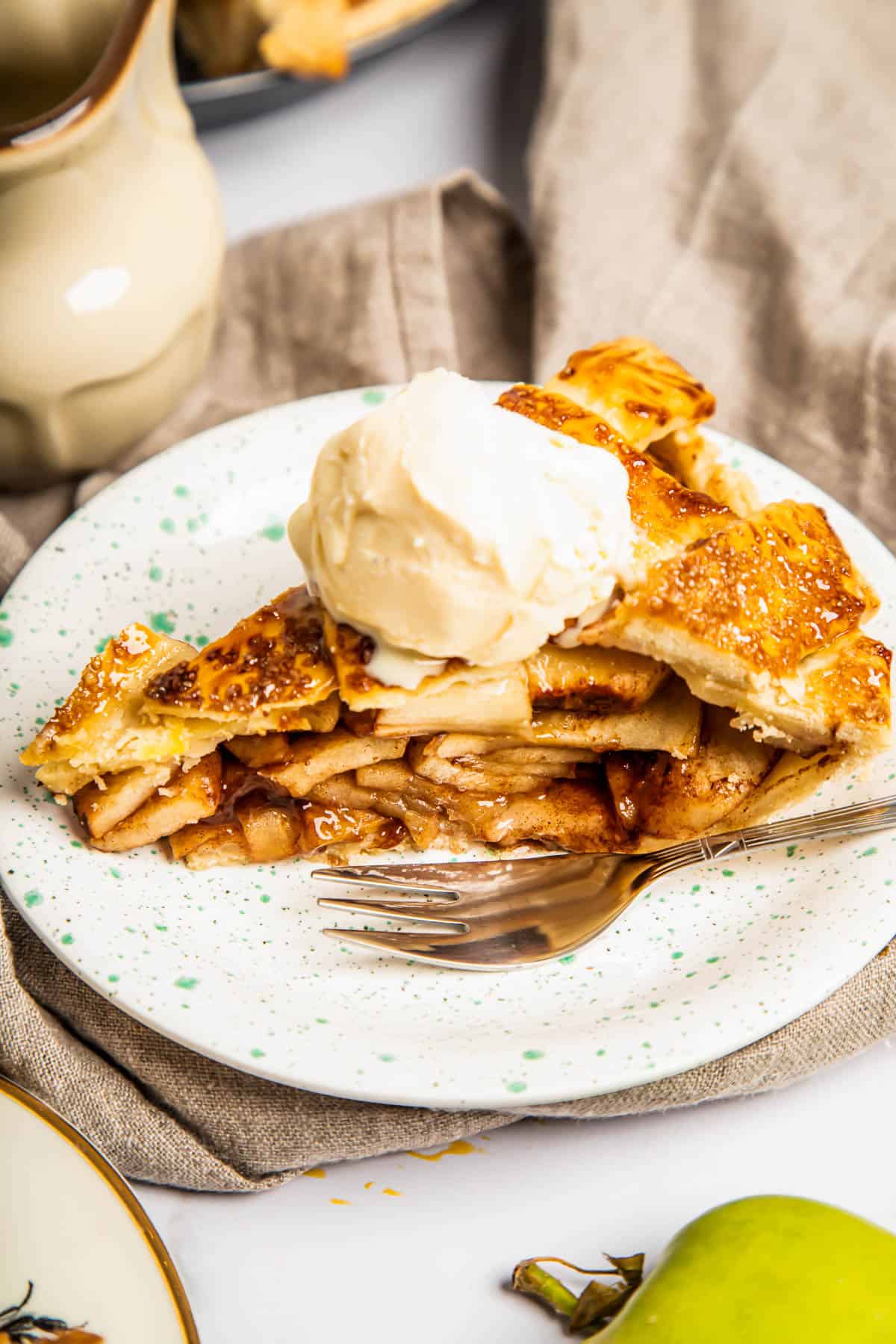 a slice of apple pie topped with ice cream on a plate with a fork