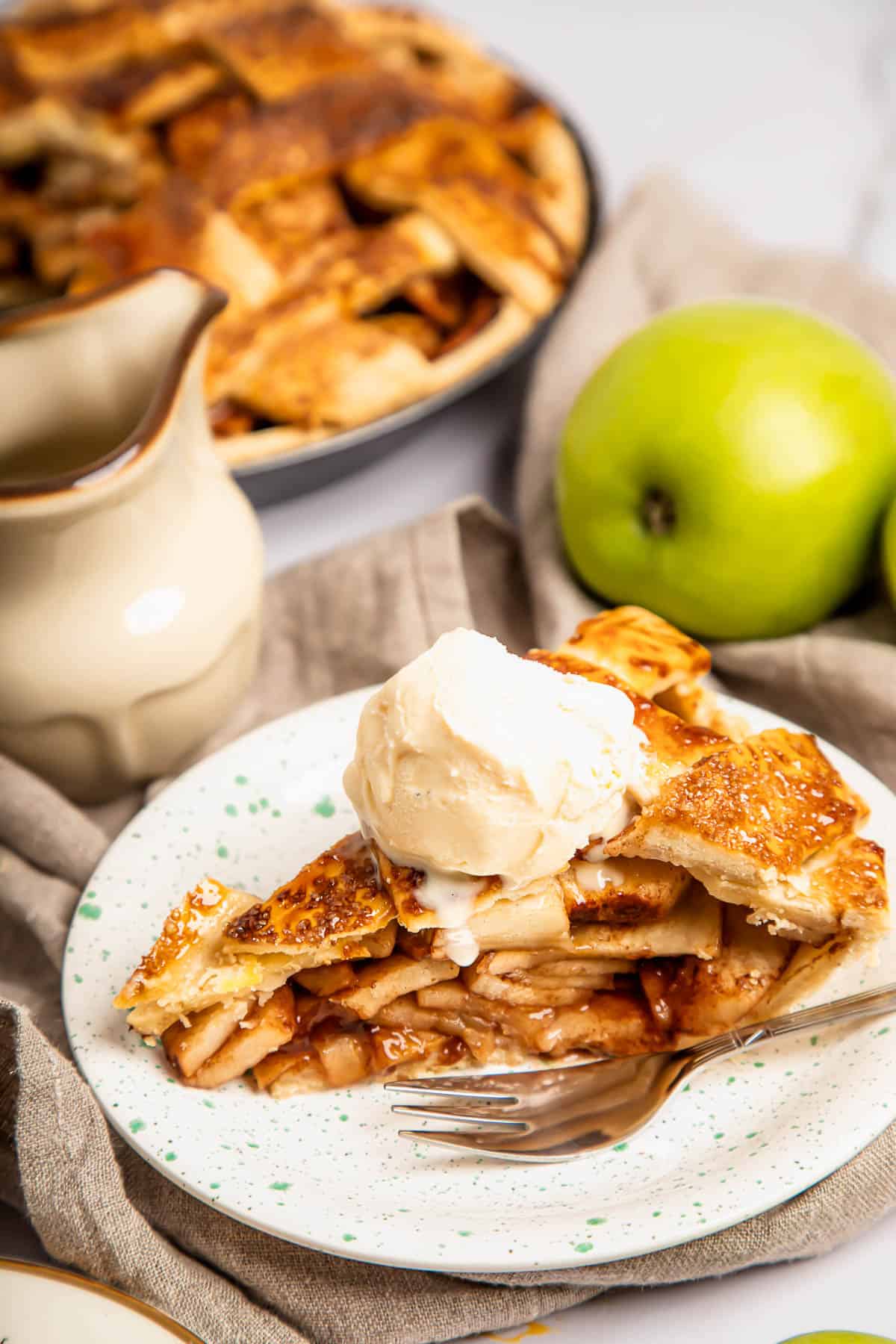 a slice of apple pie topped with ice cream on a plate with a fork