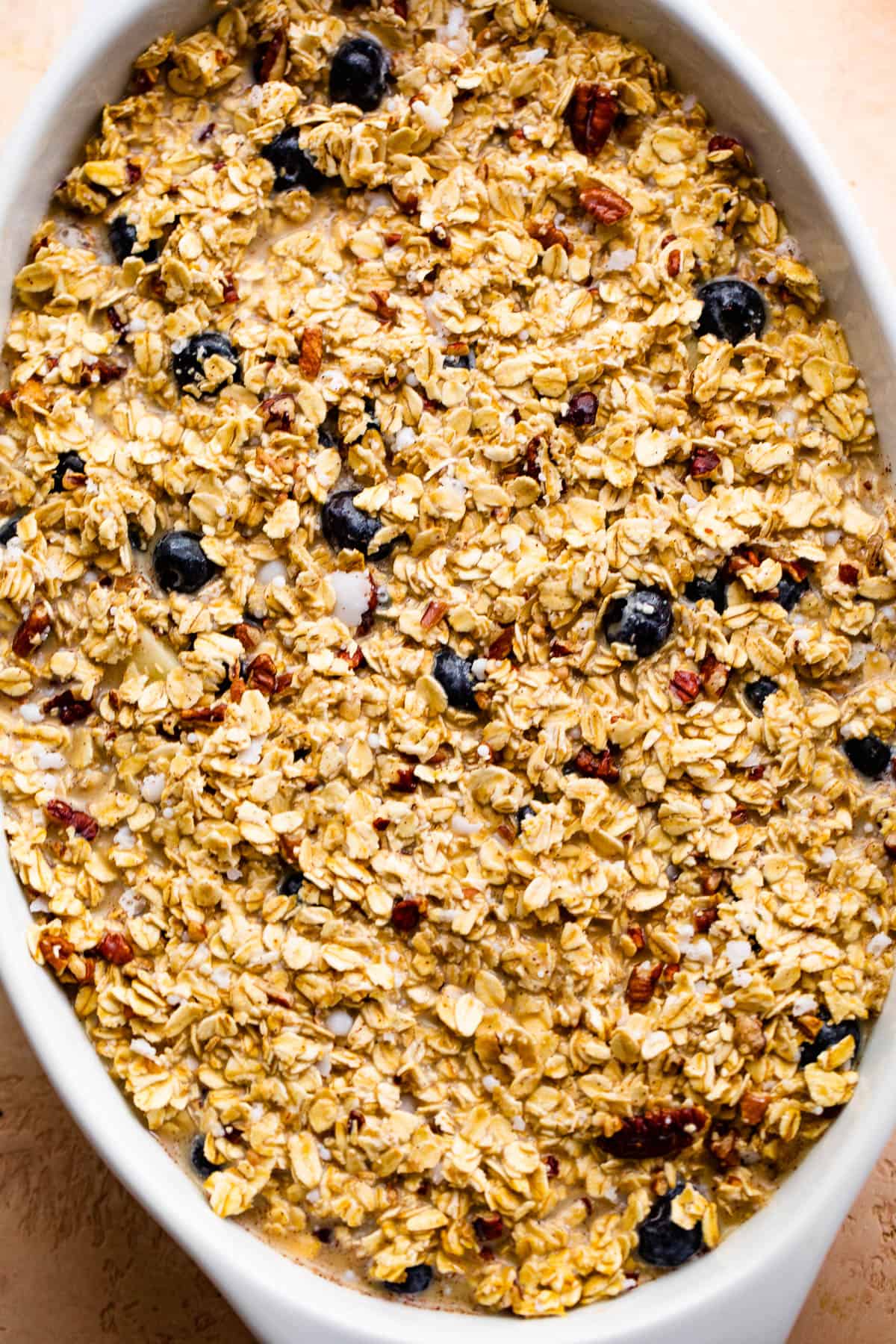 oval baking dish with uncooked oatmeal with berries and apples