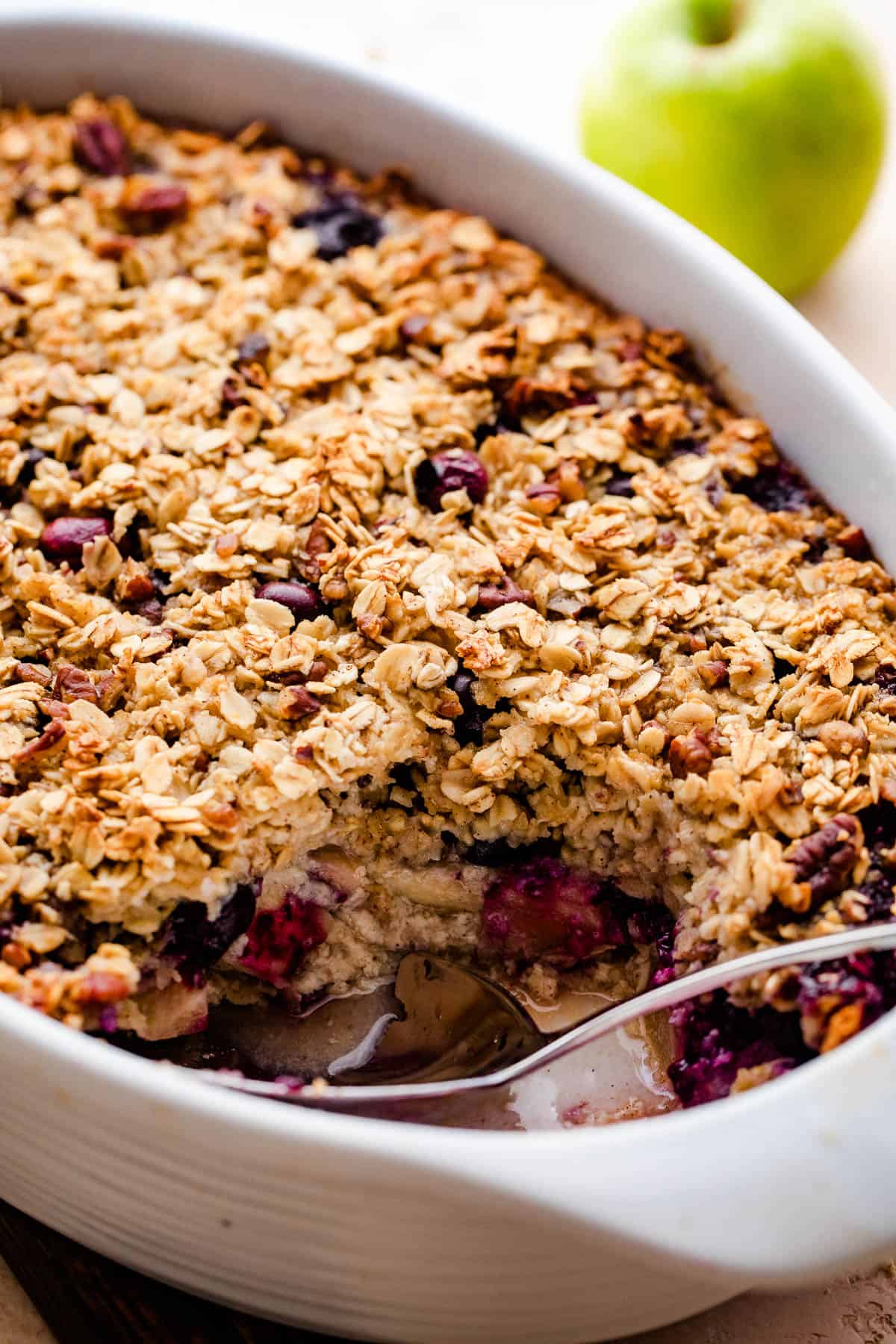 a white baking dish with baked oatmeal filled with apples and studded with blueberries.