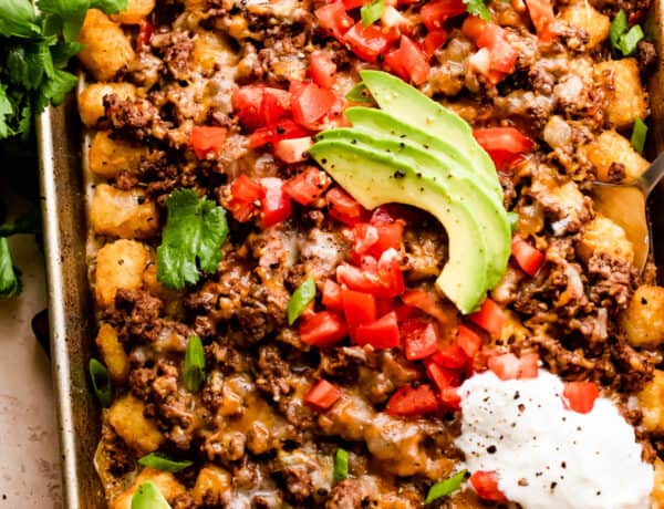 baking sheet with tater tots topped with ground beef, melted cheese, diced tomatoes, sour cream, and avocado slices