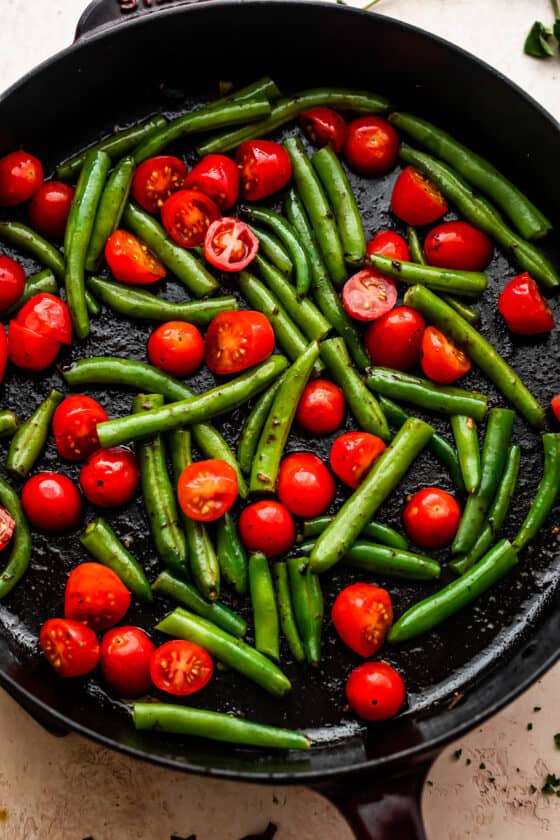 overhead shot of pan frying cherry tomatoes and green beans in a cast iron skillet