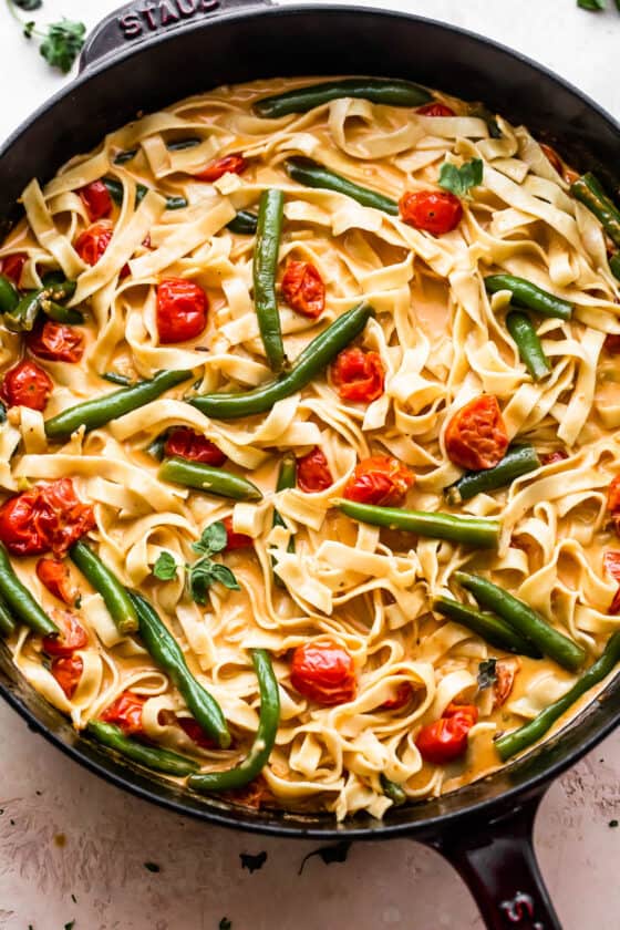 overhead shot of a skillet with fettuccine pasta in creamy sauce with tomatoes, and green beans