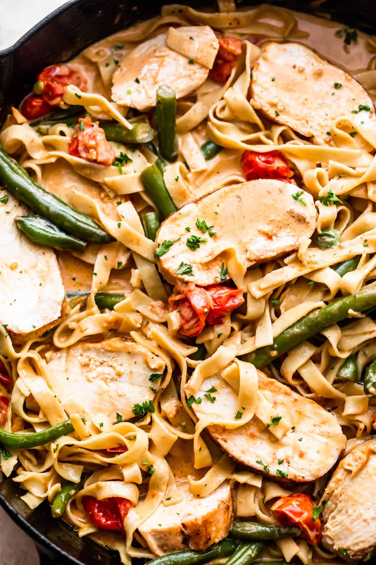 fettuccine pasta in creamy sauce with slices of blackened chicken, tomatoes, and green beans