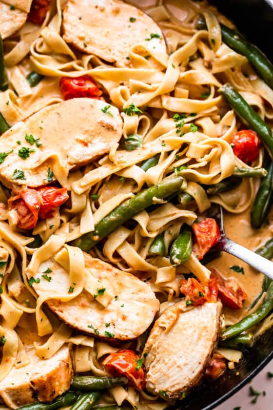 fettuccine pasta in creamy sauce with slices of blackened chicken, tomatoes, and green beans
