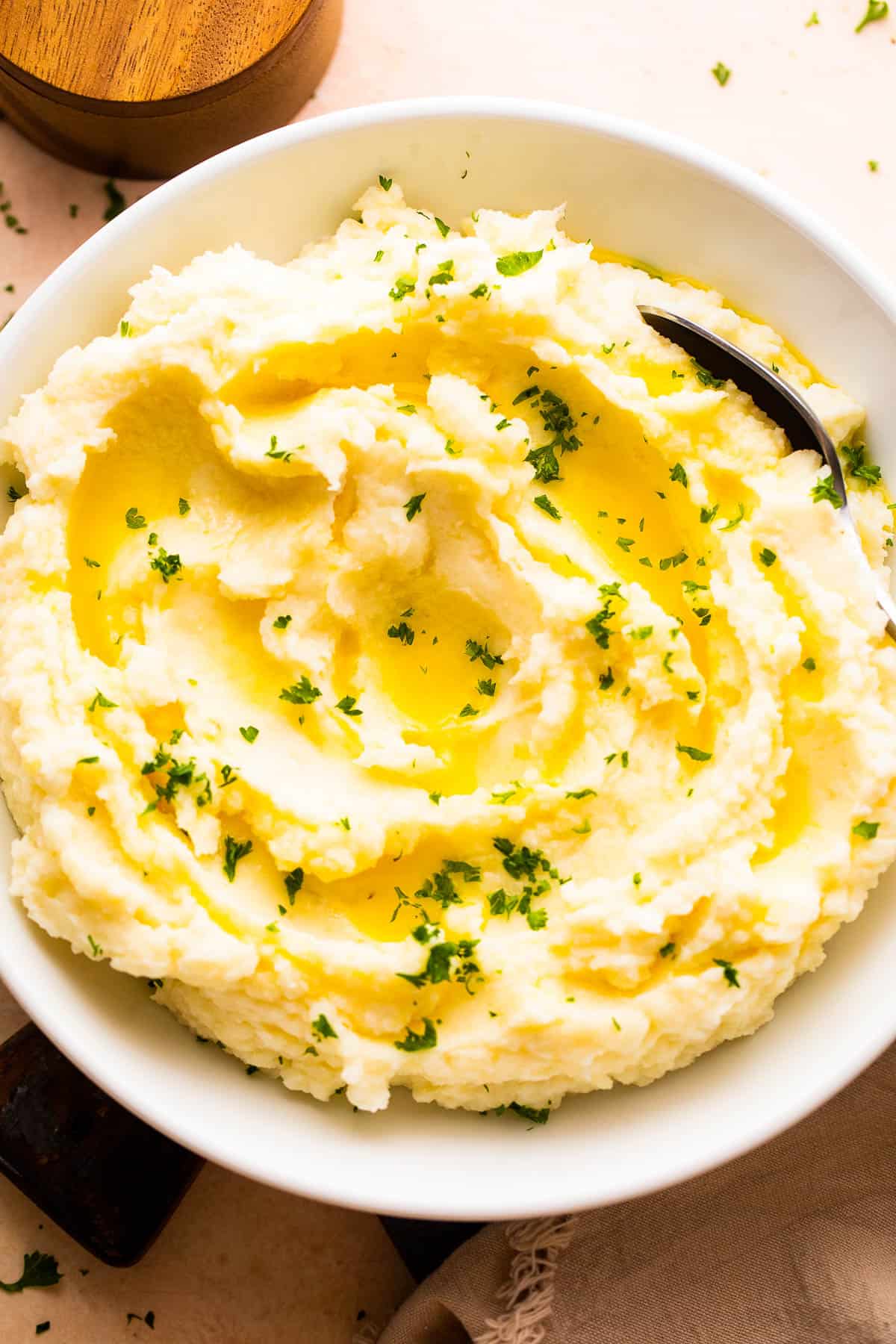 overhead shot of a bowl with creamy mashed potatoes garnished with melted butter and parsley