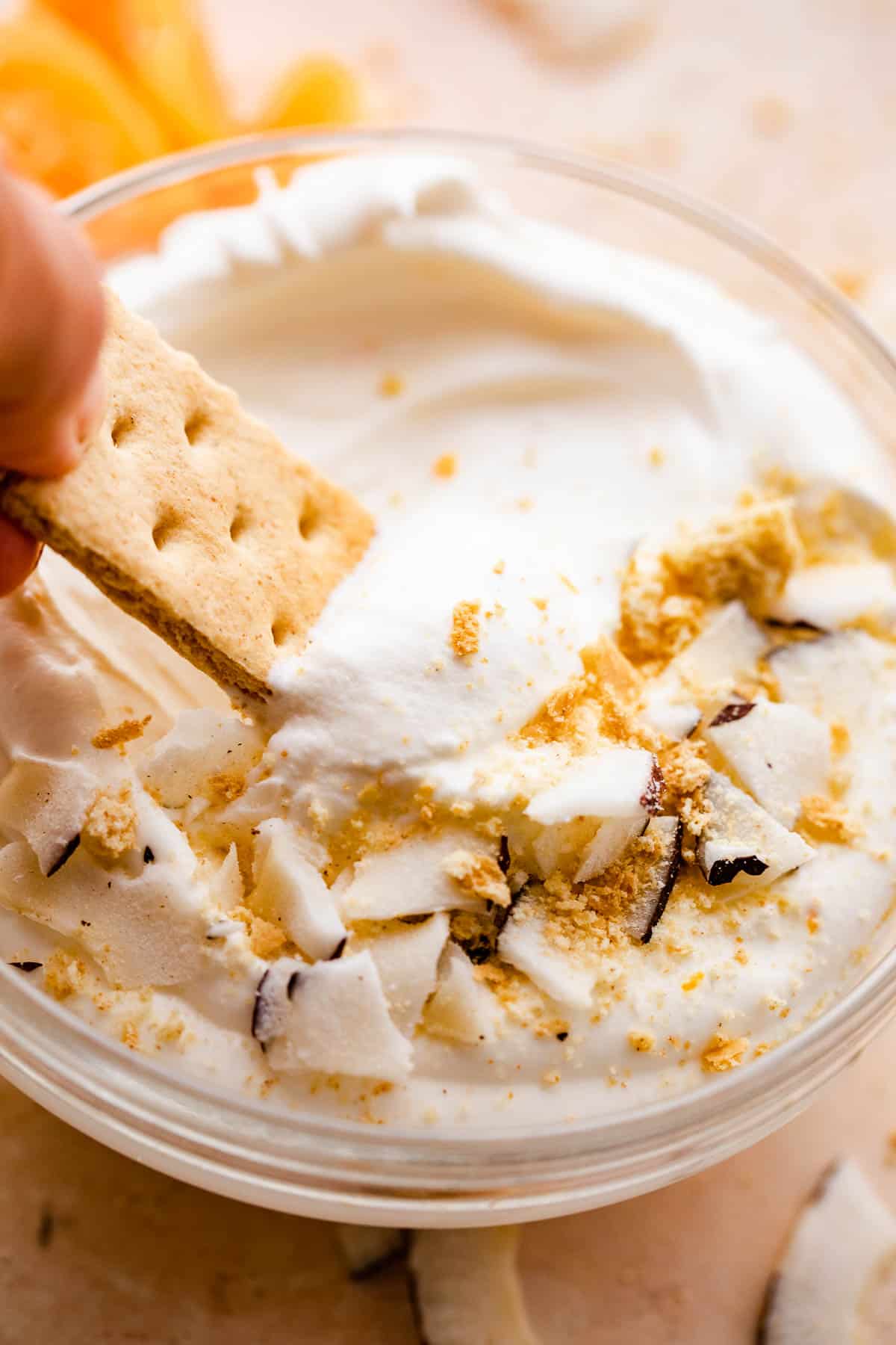 graham cracker dipping into a creamy coconut fruit dip topped with cookie crumbs and coconut shavings. 