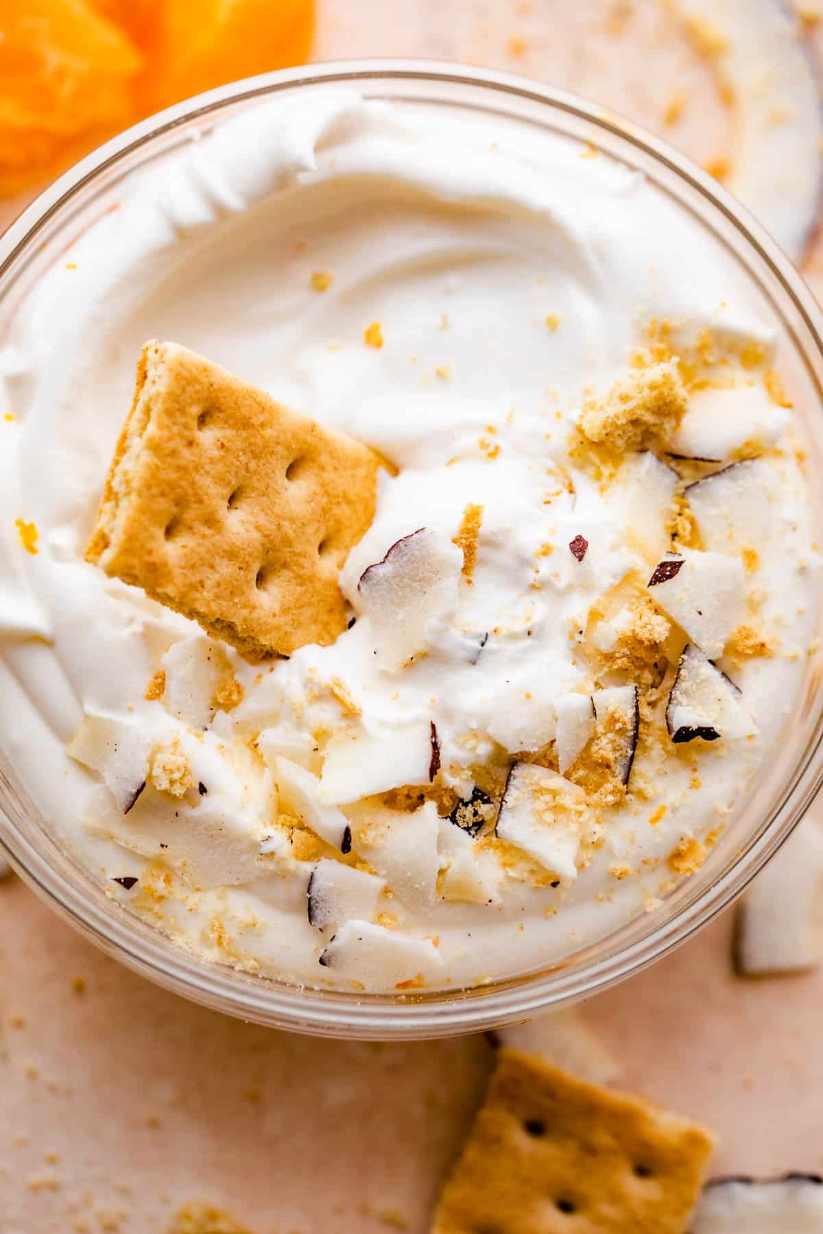 overhead shot of a creamy coconut dip served in a glass bowl with tangerine slices and coconut shavings placed around and on the sides of the bowl.