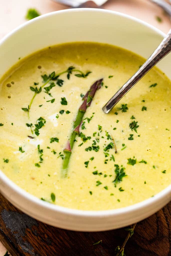 Cream of Asparagus Soup in a white bowl with a spoon inside.