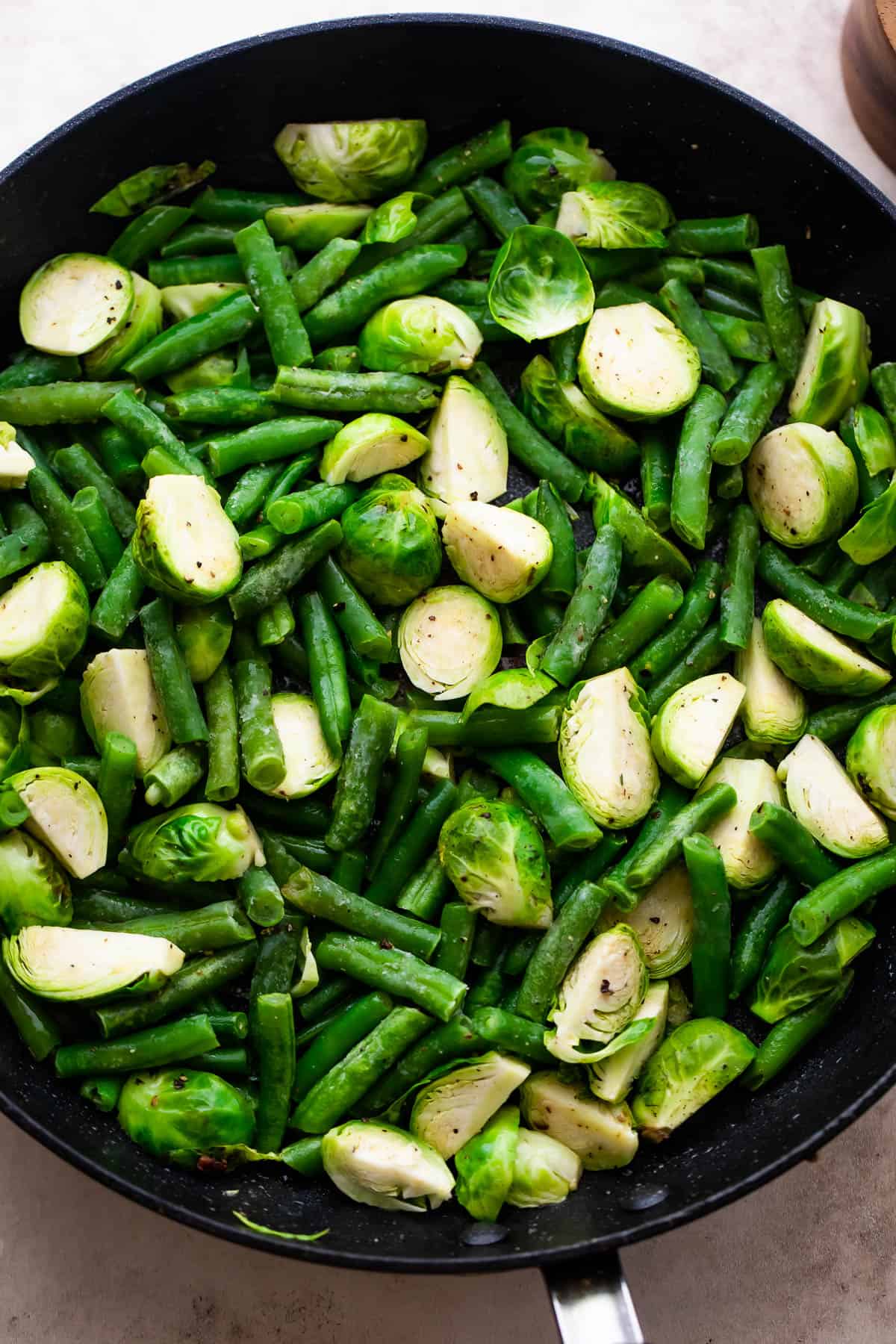 sauteeing brussel sprouts and green beans in a black skillet