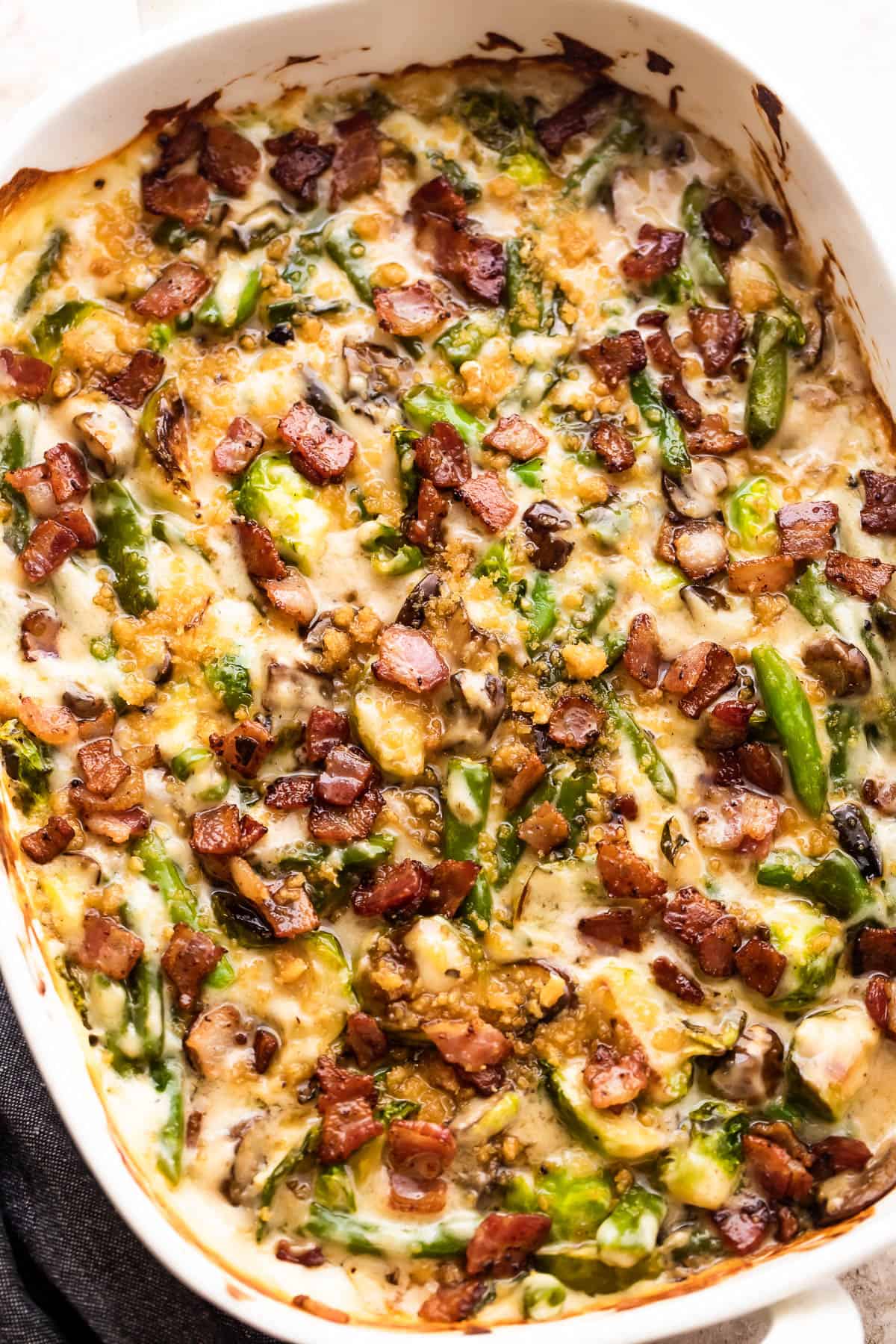 overhead shot of green bean and brussel sprouts casserole topped with diced bacon and breadcrumbs.