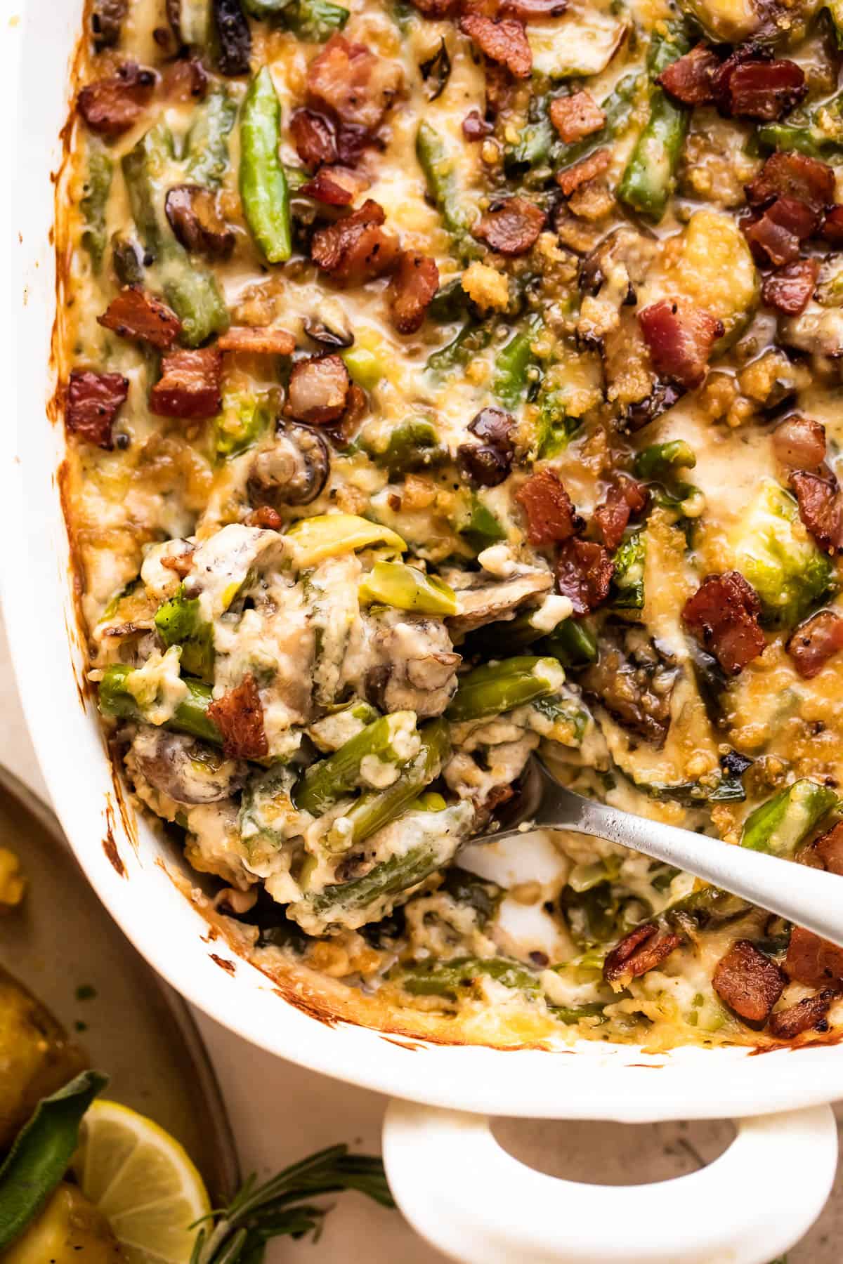 spooning out green bean casserole from a white baking dish.