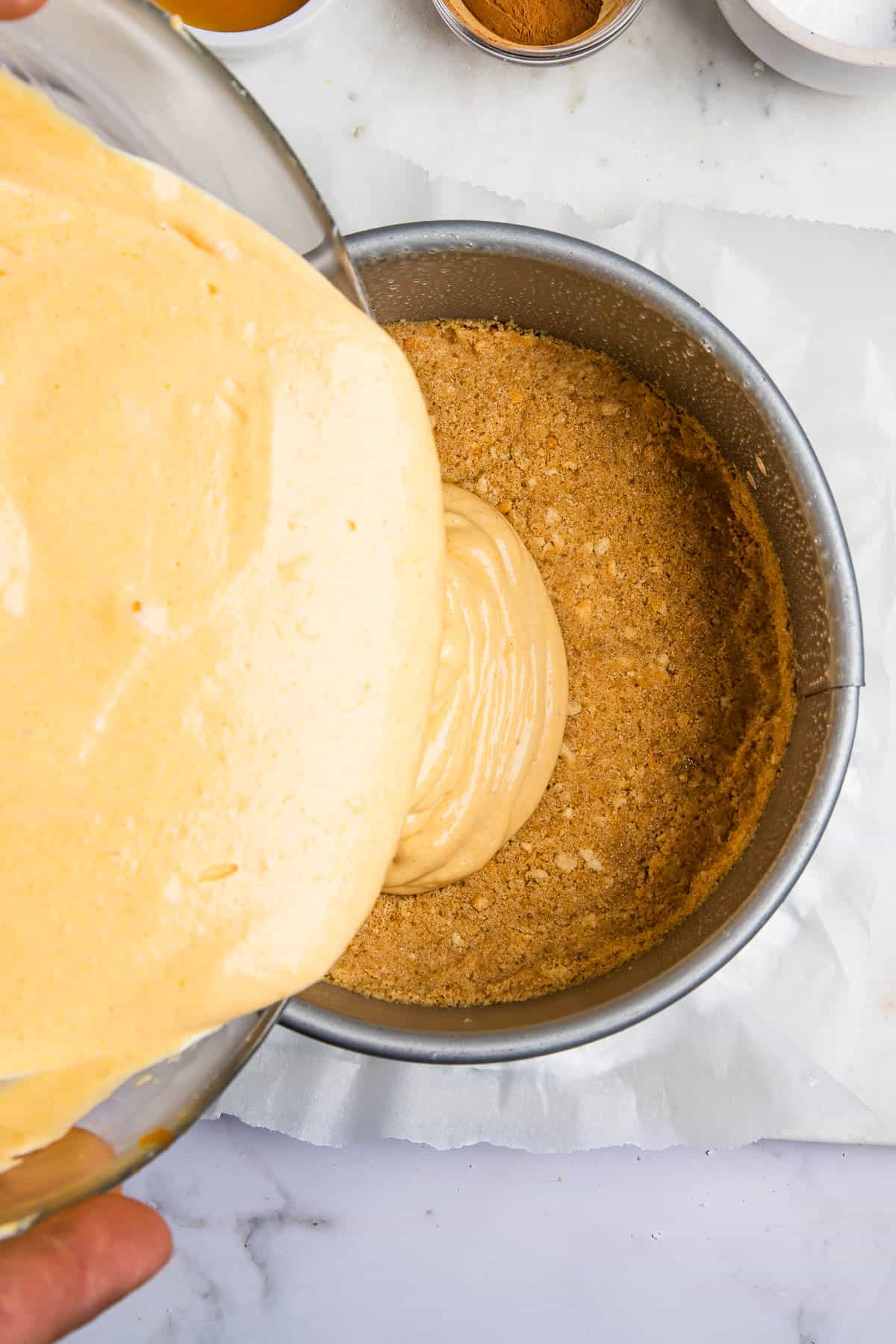pouring cheesecake batter over crust inside of an instant pot.