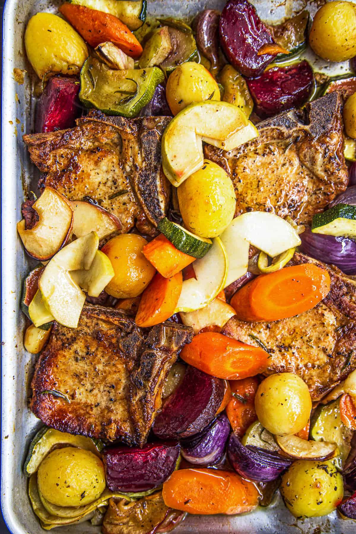 A close-up overhead shot of the baking dish with pork chops, apples, and vegetables cooked with apple juice and rosemary.