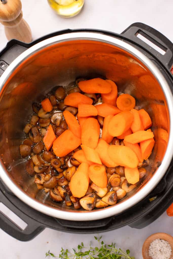 Mushrooms and carrot pieces browning in the bottom of an Instant Pot.