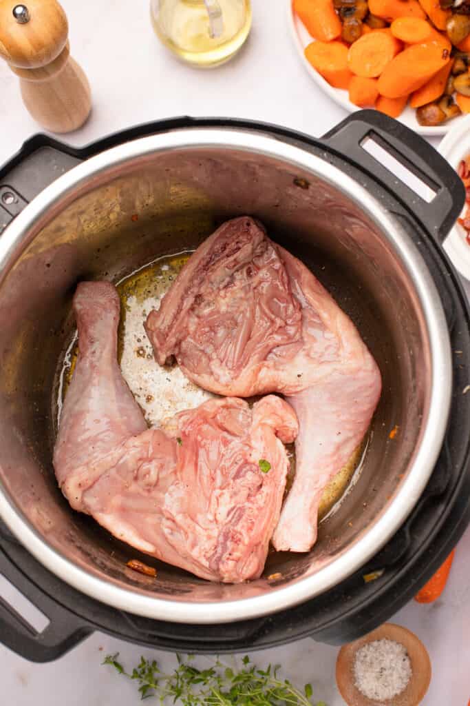 Marinated chicken legs frying in the bottom of an Instant Pot.