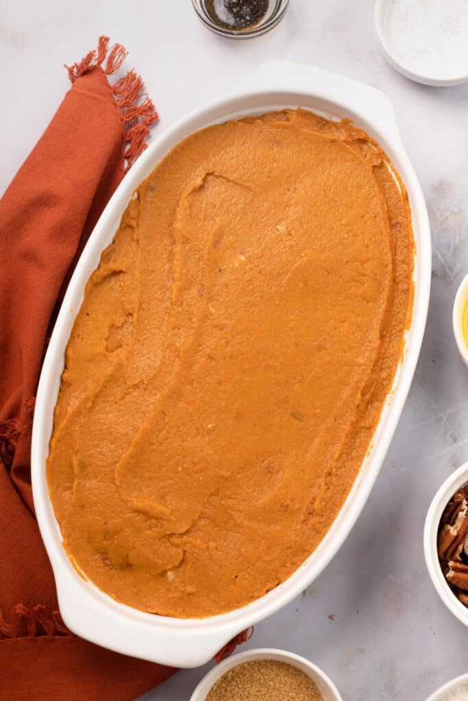 A baking dish with unbaked sweet potato casserole mixture spread inside.